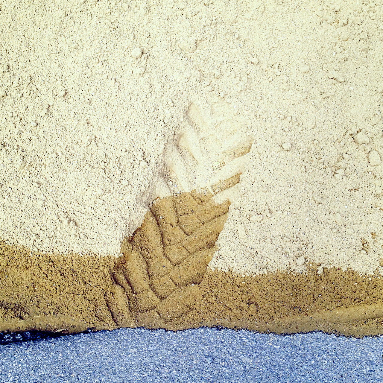 das untere Zehntel des Bilds zeigt eine Teeroberfläche, auf der ein gelblicher Sandhaufen liegt. Die Spur eines Gabelstaplers drückt sich im feuchten Sand ab.