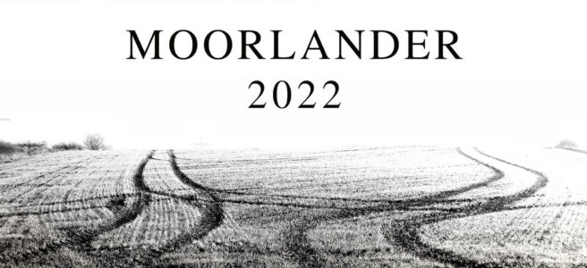Kalenderdeckblatt mit der Aufschrift Moorlander 2022 zwischen düsterem Himmel und einer Ackerszene zweier sich zunächst annähernder, dann parallel verlaufender Traktorspuren im Stoppelacker.